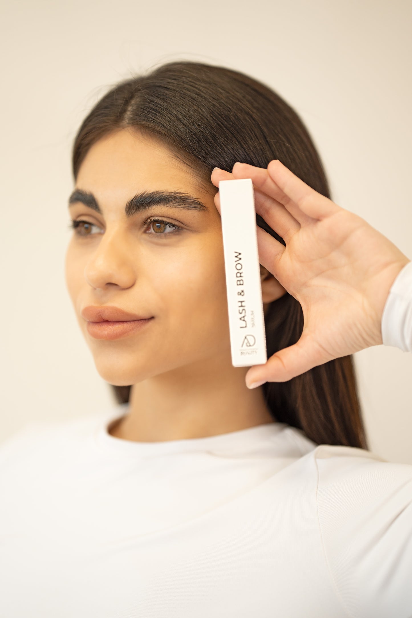 Frau hält AD Beauty Lash & Brow Serum an ihr Gesicht – hormonfreies Wimpernserum für empfindliche Haut und natürliche Pflege. Pflegendes Wimpernserum.